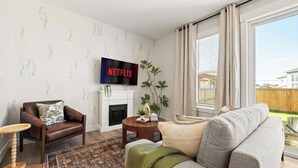 Ein Wohnzimmer mit Kamin, einer Couch, einem Sessel, einem Couchtisch und einem Fernseher, der 'NETFLIX' anzeigt.