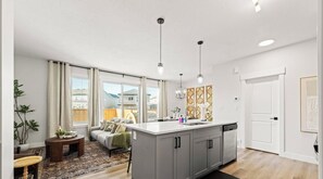 Een moderne keuken met een centraal eiland, hangende verlichting en uitzicht op het buiten.