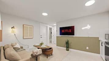 A modern living room with a sofa, a dining table, and a wall-mounted television displaying the Netflix logo.