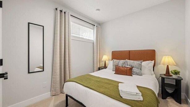 Een hotelkamer met een bed, twee nachtkastjes, een raam met gordijnen, een spiegel aan de muur en een bedlampje.