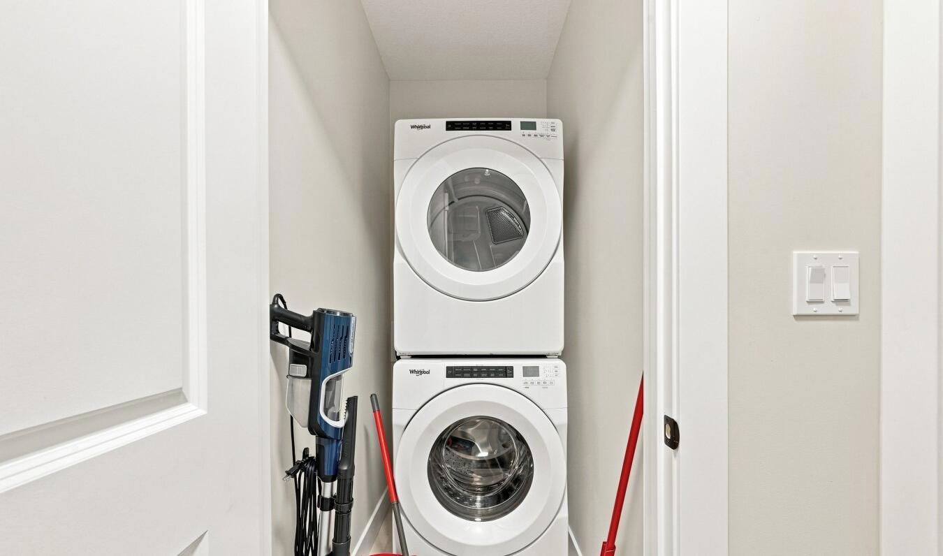 A laundry room with two stacked washing machines and a hose.
