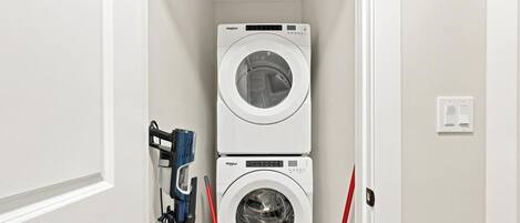 A laundry room with two stacked washing machines and a hose.