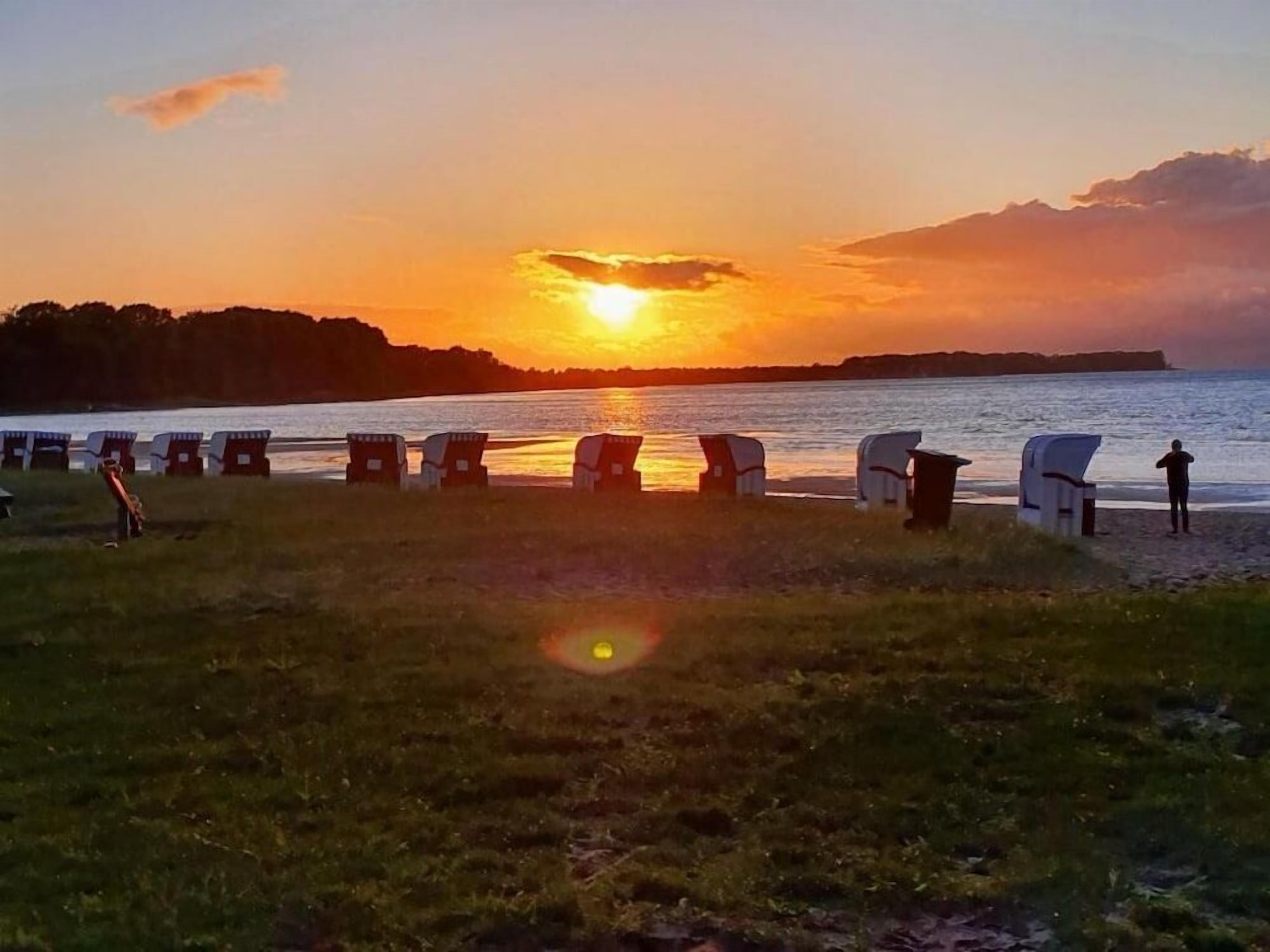 A sunset view over a body of water with beach chairs lined up facing the water.