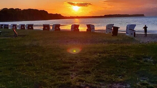 En vacker solnedgång över ett vattenområde, med strandstolar uppradade och vända mot vattnet.