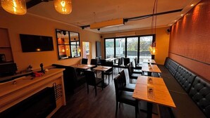 En restauranglokal med bord, stolar, en bardisk och ett stort fönster.
