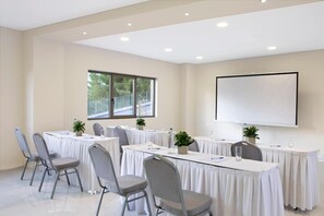 A conference room with a large screen, multiple tables, and chairs, equipped with water bottles and pens. - Zeus Eleva Ajul, a Registry Collection Hotel (Kassandra)