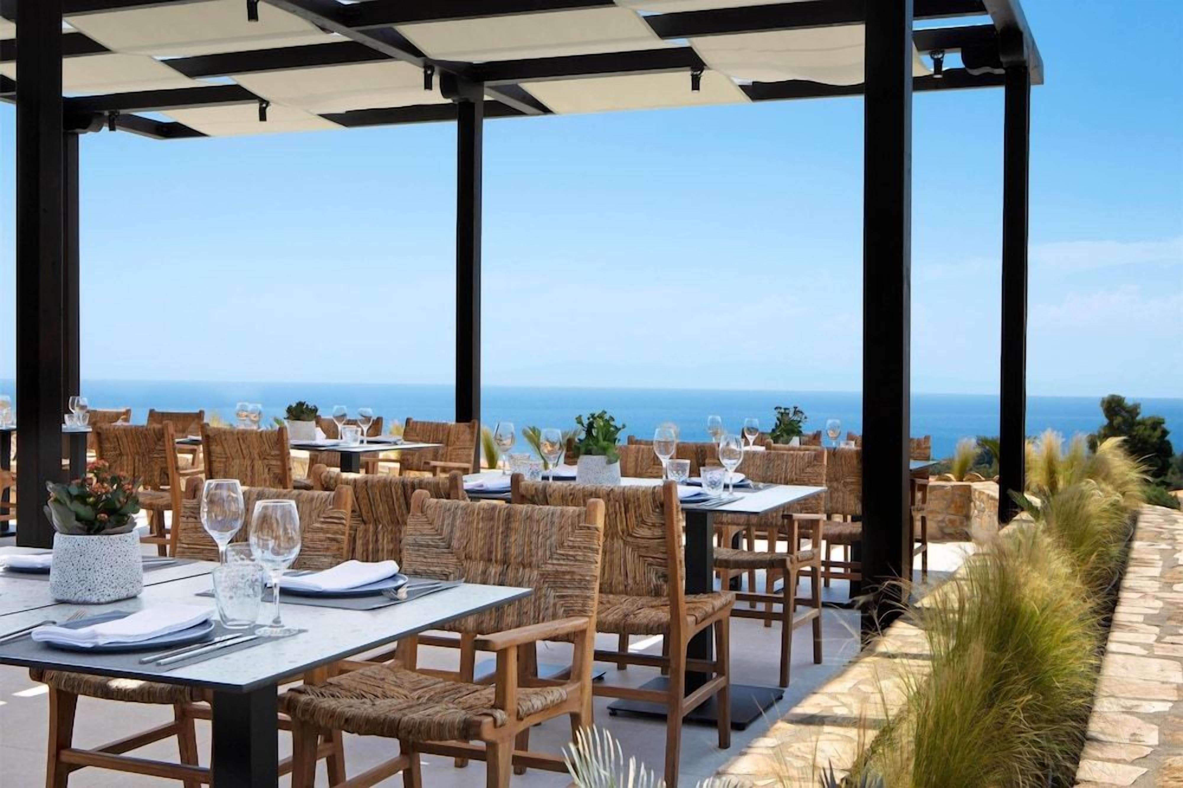 Un área de comedor al aire libre con mesas y sillas, con vista al litoral.