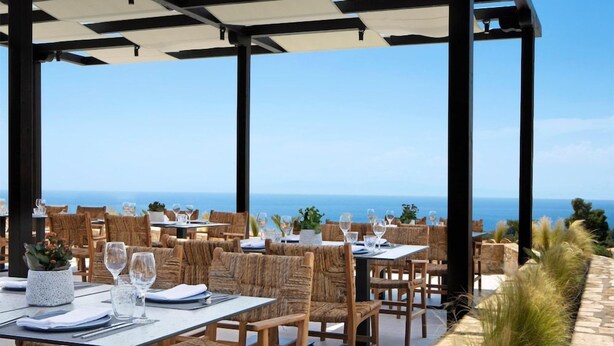 An outdoor dining area with tables and chairs, overlooking a coastal view.