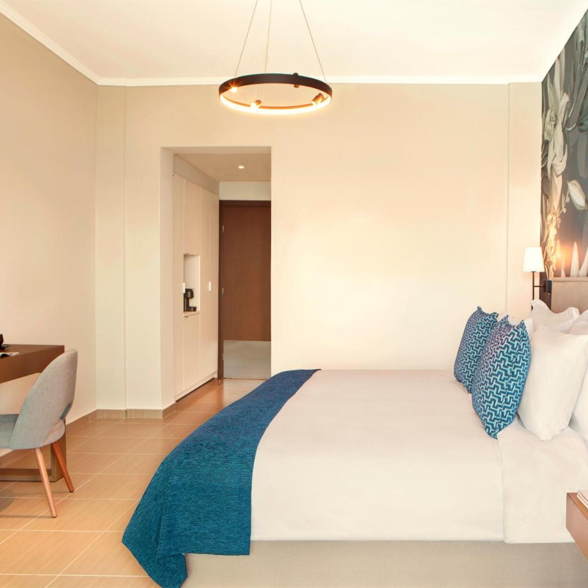 Une chambre d’hôtel avec un grand lit, un bureau avec une chaise, une machine à café et un tableau au mur.