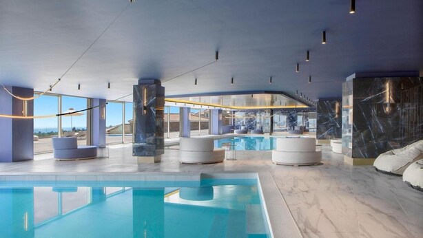 A modern indoor swimming pool with clear glass walls, a marble floor, and contemporary seating areas. - Zeus Eleva Ajul, a Registry Collection Hotel (Kassandra)