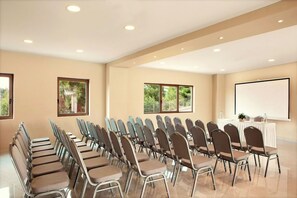 A conference room with rows of chairs, a projector screen, and a table with water bottles.