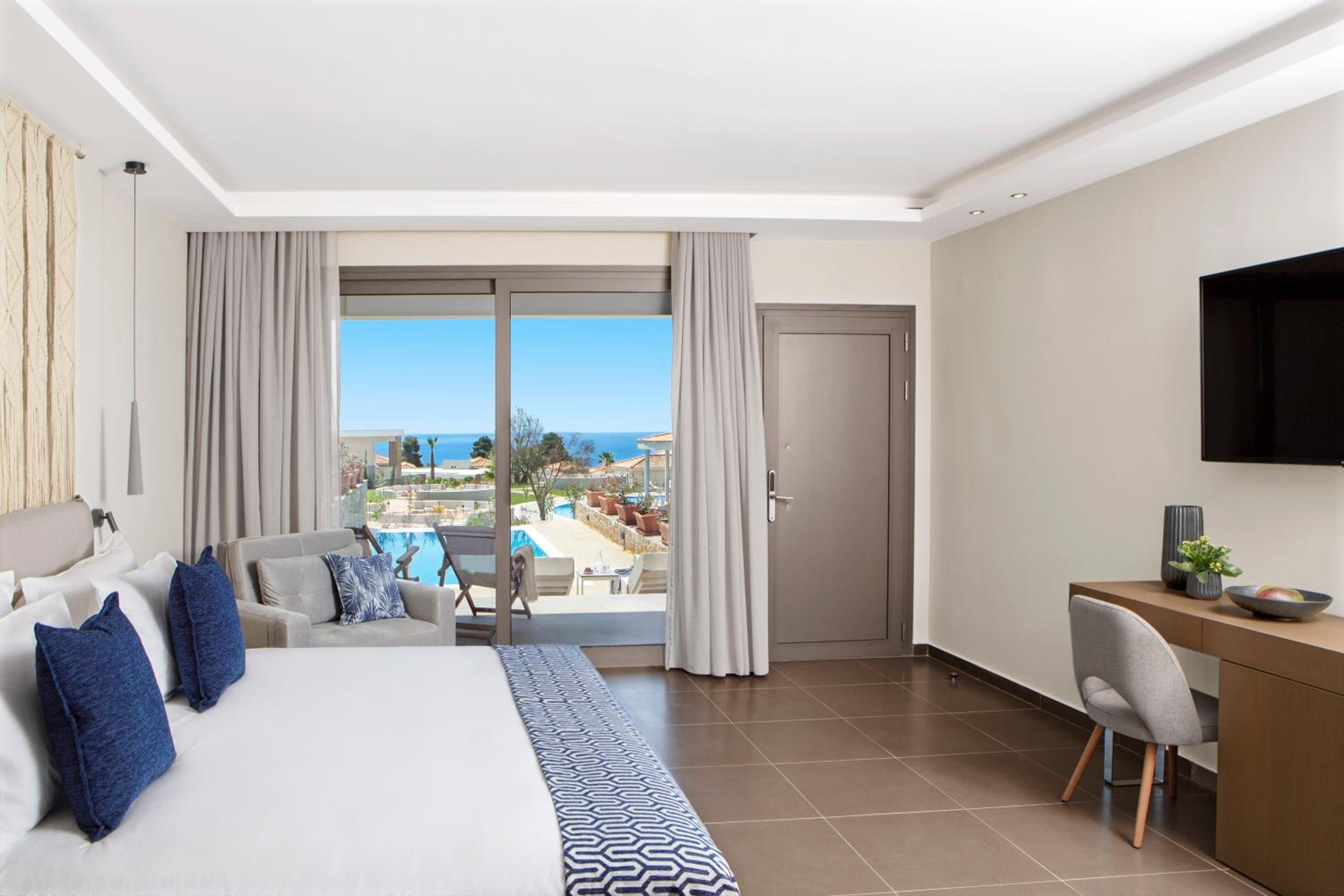 Une chambre d’hôtel équipée d’un lit, d’un bureau, d’une chaise, d’une télévision et offrant une vue sur une piscine et un paysage.