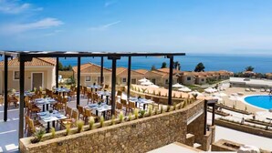 A rooftop dining area with tables and chairs, overlooking a swimming pool and the sea. - Zeus Eleva Ajul, a Registry Collection Hotel (Kassandra)