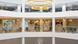 A multi-level atrium with a modern design, featuring a central light fixture, seating areas, and a fountain. - Zeus Eleva Ajul, a Registry Collection Hotel (Kassandra)