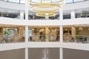 A multi-level atrium with a modern design, featuring a central light fixture, seating areas, and a fountain. - Zeus Eleva Ajul, a Registry Collection Hotel (Kassandra)