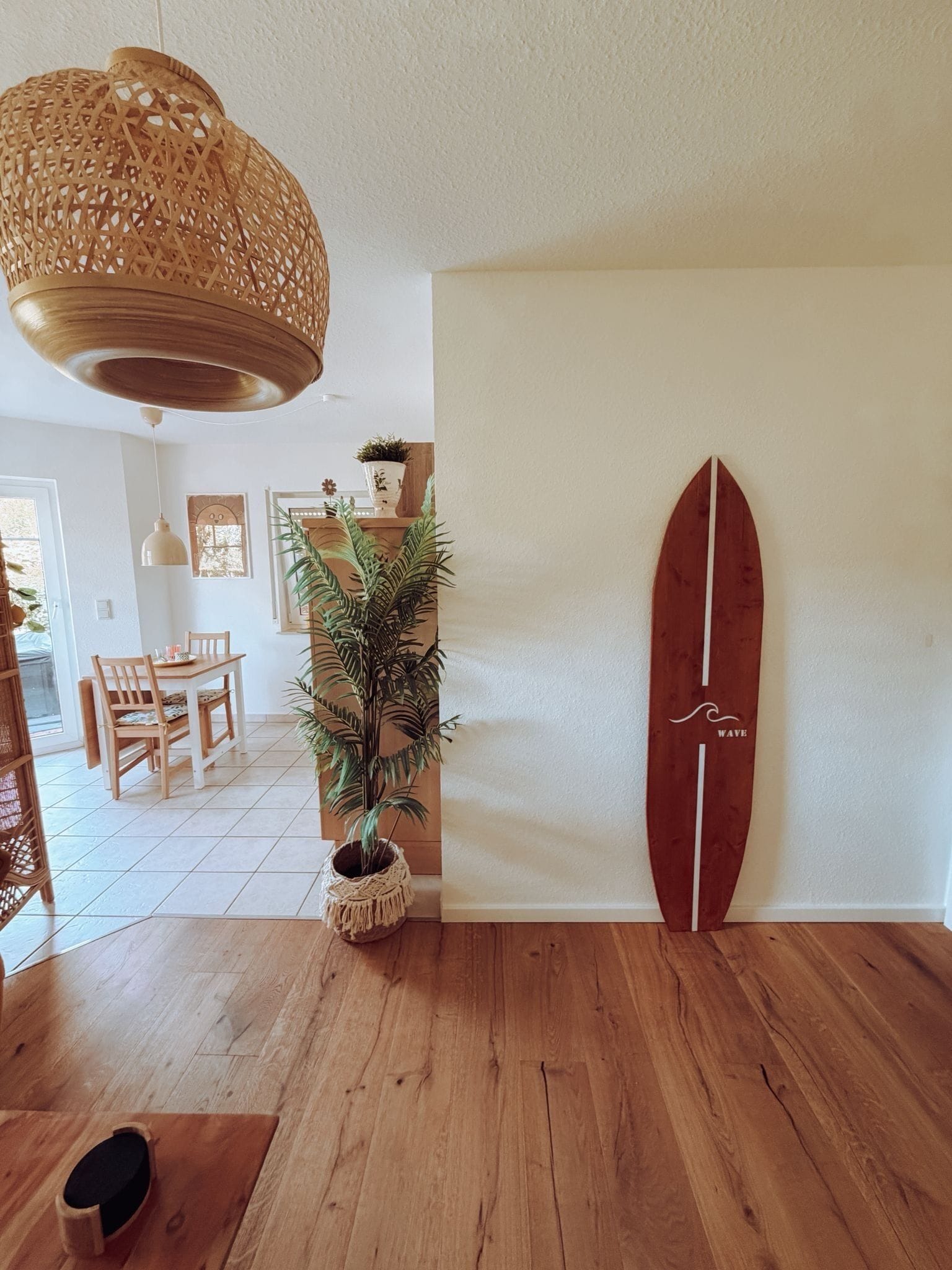 Ein Zimmer mit Holzboden, einem an der Wand lehntes Surfbrett, einer hängenden Gewebedecke und einem Blumentopf.