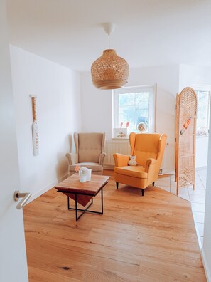 Un salon moderne avec un plancher en bois, un fauteuil beige, une table basse en bois, un luminaire suspendu et une fenêtre donnant sur un beau paysage.