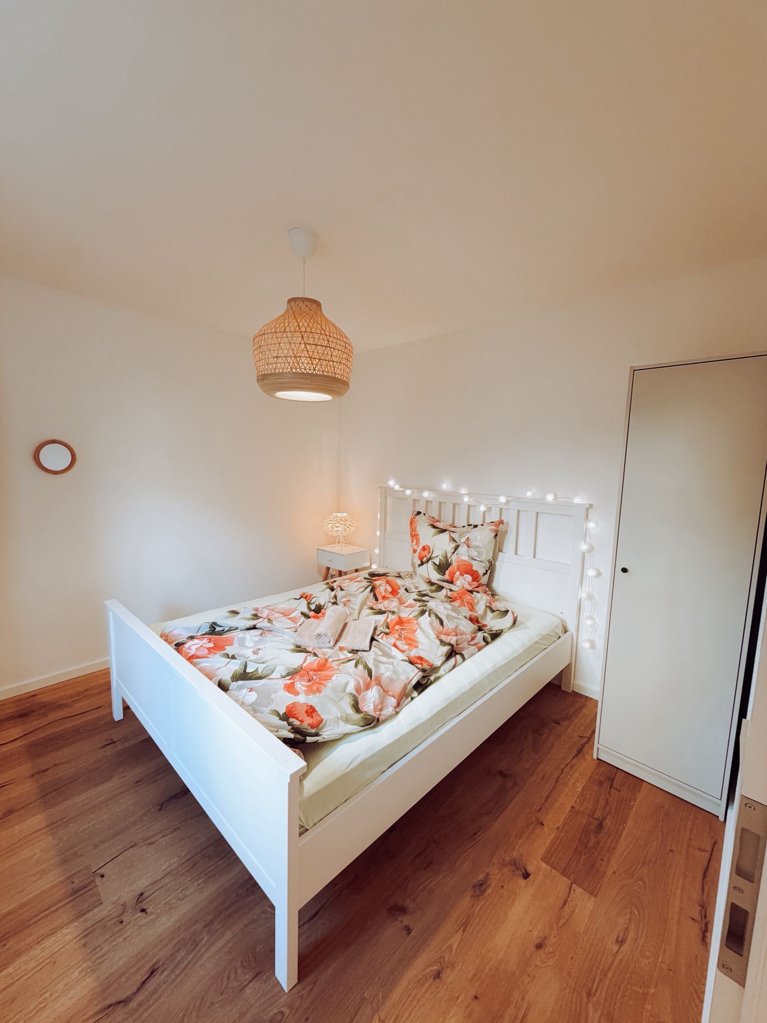 Ein Schlafzimmer mit einem weißen Bett, Holzboden, einer Hängelampe und einem Kleiderschrank.