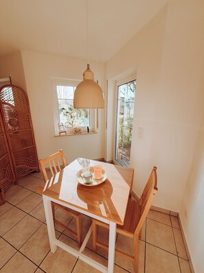 Een eethoek met een tafel, stoelen, een hanglamp en een raam met uitzicht op bomen.