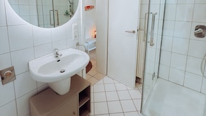 Ein modernes Badezimmer mit einem weißen Waschbecken, einem Spiegel und einer Duschkabine aus Glas.