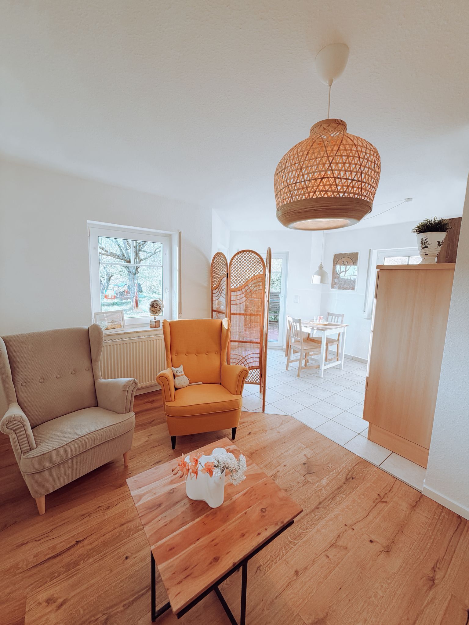 Ein Wohnzimmer mit Sofa, Sessel, Couchtisch aus Holz und einer Pendelleuchte.