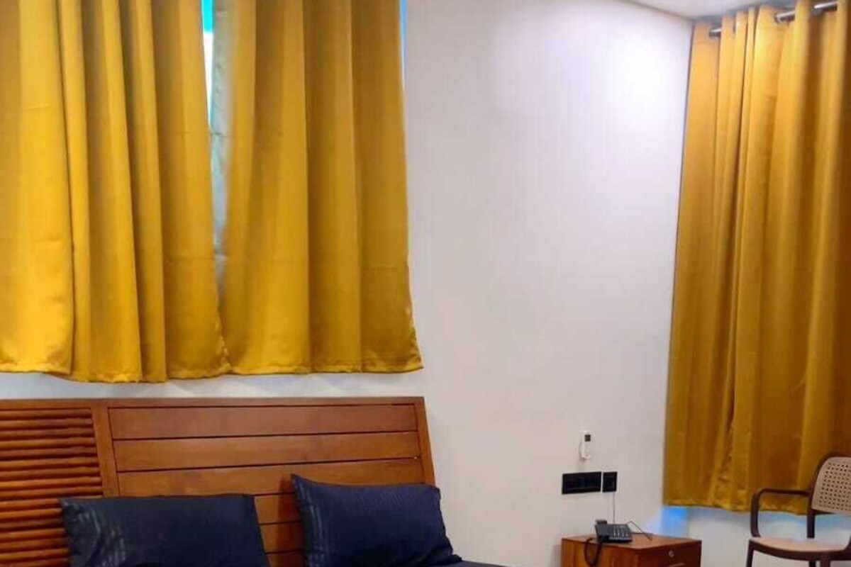 A bedroom with a wooden bed, a nightstand, a chair, and yellow curtains.