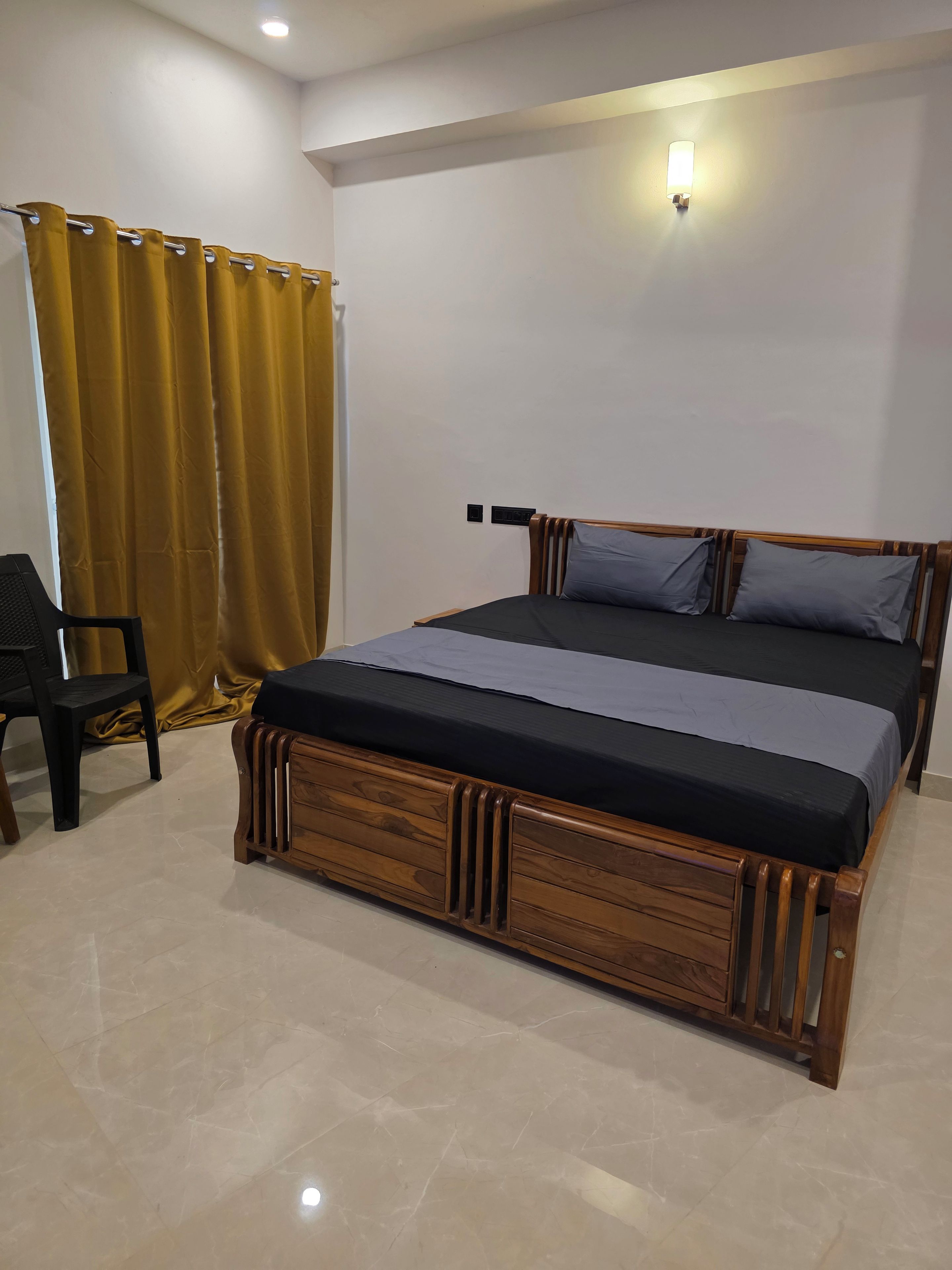 Quarto com cama de madeira, uma cadeira e cortina.