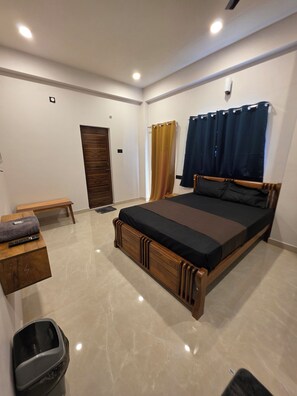 Un dormitorio con una cama grande, un banco, un cubo de basura y una puerta.