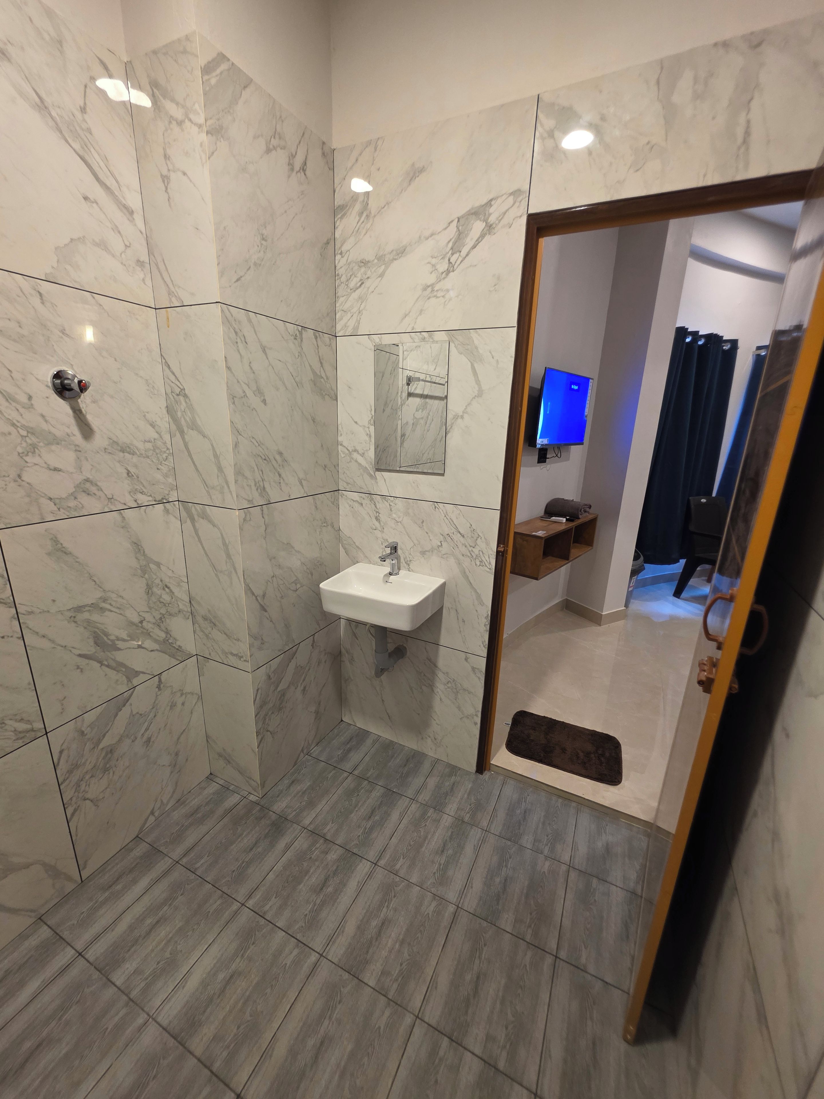 A bathroom with marble walls, a white sink, and a wooden floor.