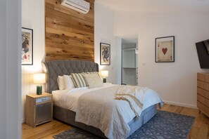 Ein Schlafzimmer mit einem Bett, Nachttischen, einer Holzwand und Kunstwerken an den Wänden.