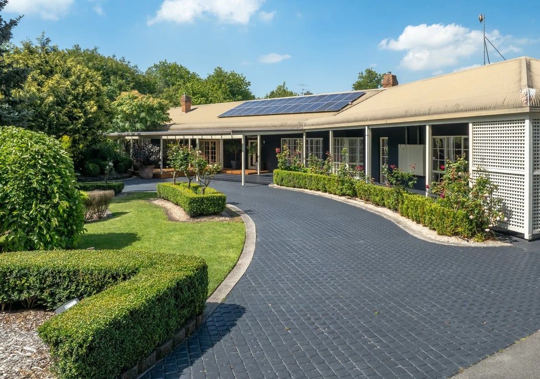 Ein Gebäude mit überdachtem Gang, Solaranlage auf dem Dach und einem angelegten Garten mit Hecken und Sträuchern.