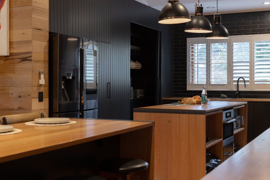 A modern kitchen with dark cabinetry, a wooden island, and pendant lighting.