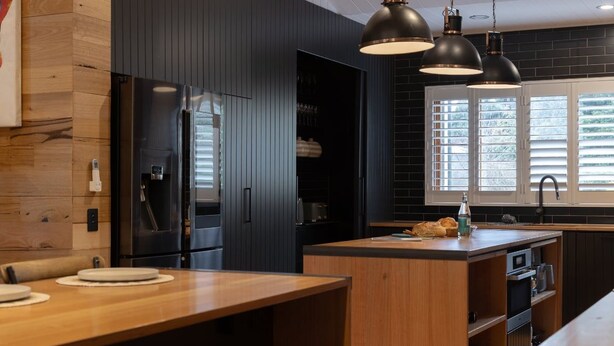 A modern kitchen with dark cabinetry, a wooden island, and pendant lighting.