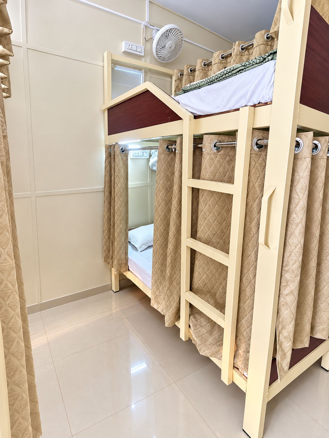 Una cama individual superpuesta con escalera, un ventilador y cortinas.