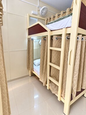 Una cama individual superpuesta con escalera, un ventilador y cortinas.