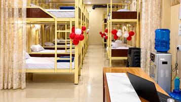 A hotel room with bunk beds, a desk with a laptop, a water dispenser, and a shower area.
