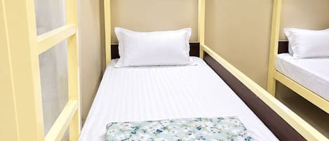 A single bed with a floral bedspread, a bedside fan, and a window with curtains.