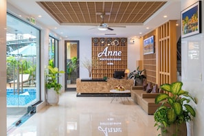 Un vestíbulo de hotel con recepción, zona de piscina y área de descanso con plantas.
