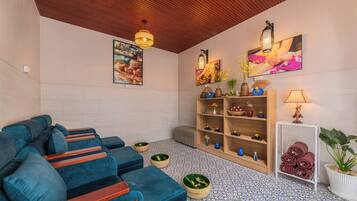 A modern lounge area with a blue sofa, wooden shelves with decorative items, and a tiled floor.