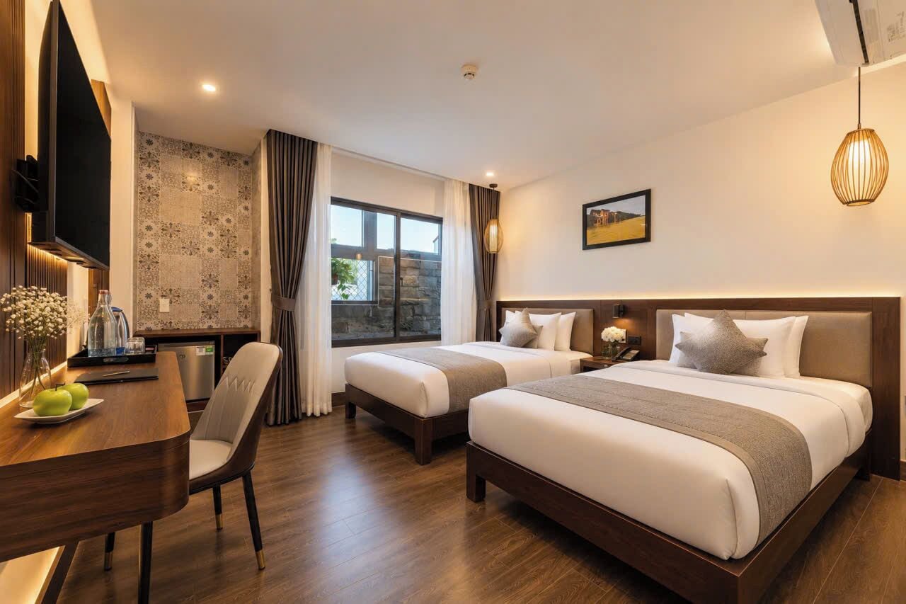 Ein Hotelzimmer mit zwei Betten, einem Esstisch mit Stühlen, einem Fernseher und einem großen Fenster mit Vorhängen.