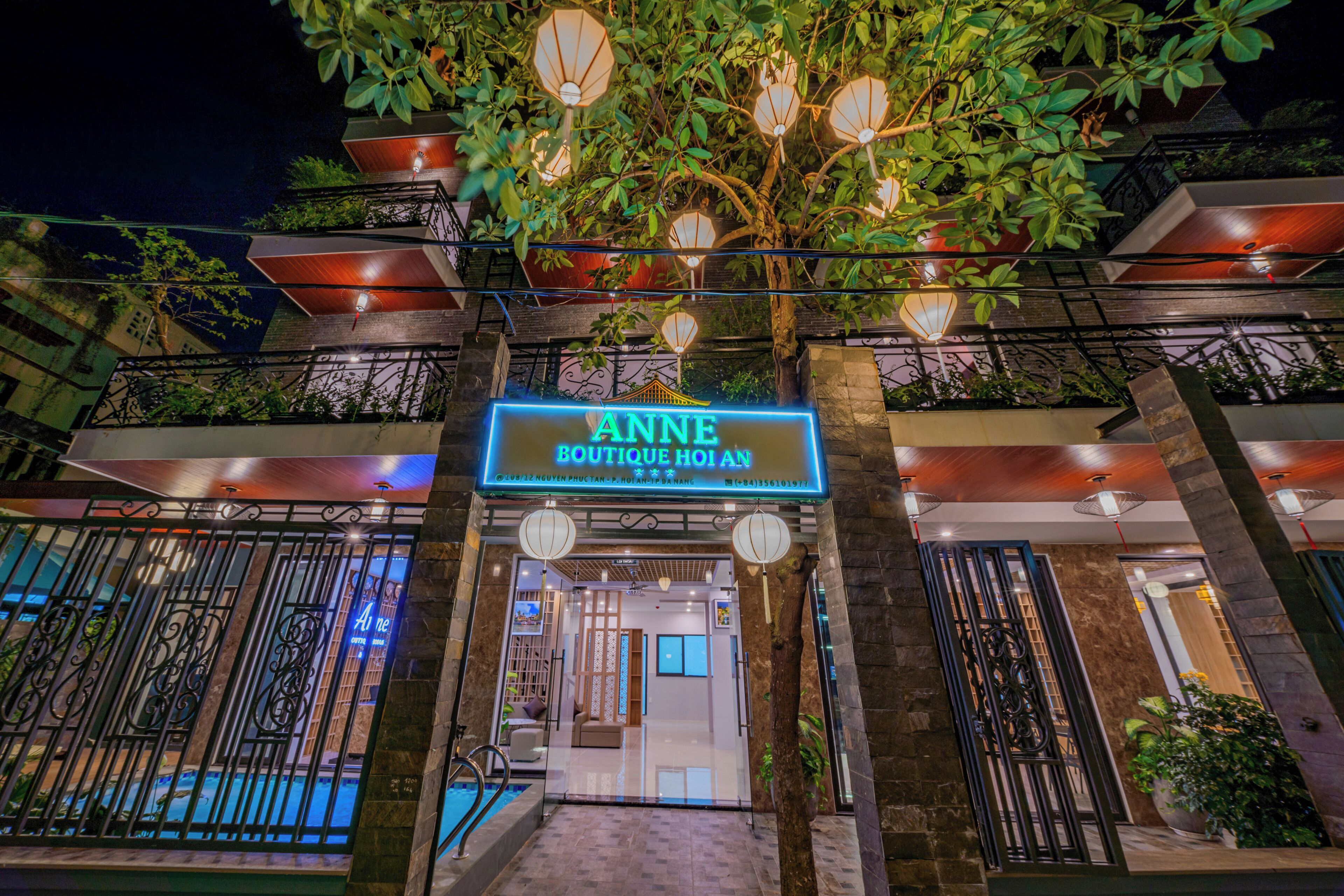 A hotel entrance with a neon sign, a pool area, and outdoor lighting.