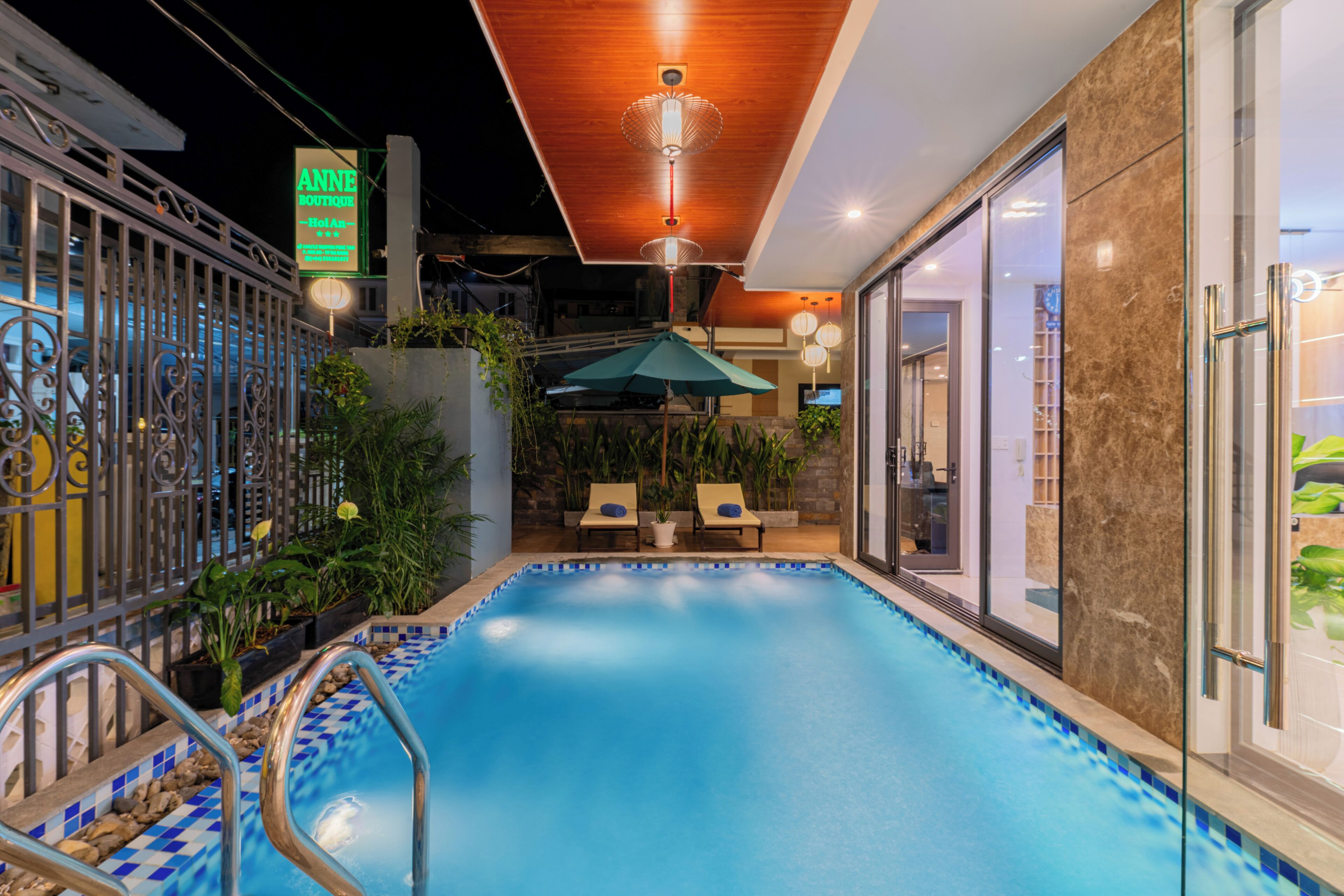 A swimming pool with a tiled edge, a lounge area with two chairs and a table, and a sign for 'ANNE BOUTIQUE.'
