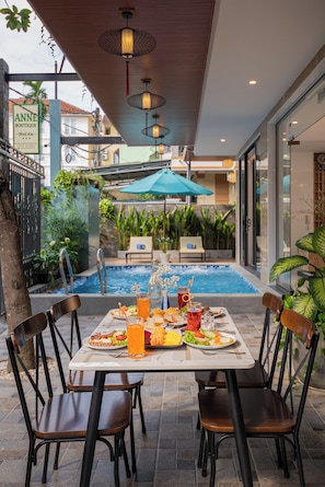 Un espacio al aire libre con zona de comedor, piscina, sillas y mesa lista para una comida.