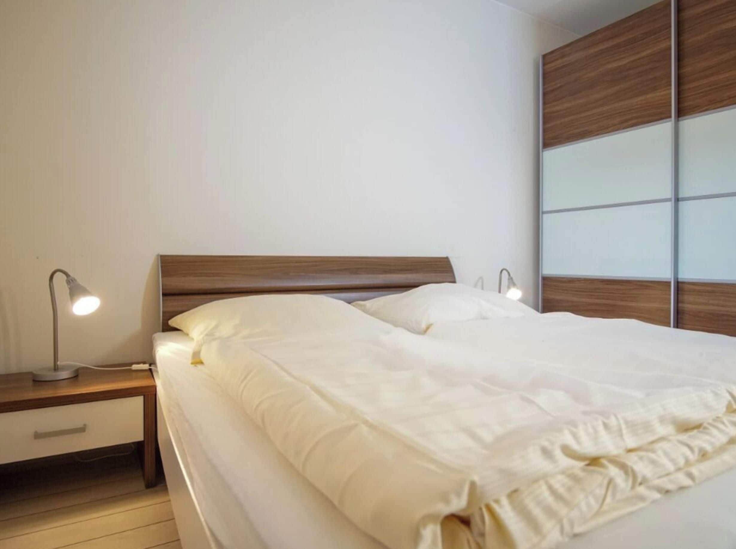 A neatly made bed with white bedding, a wooden headboard, and bedside lamps.