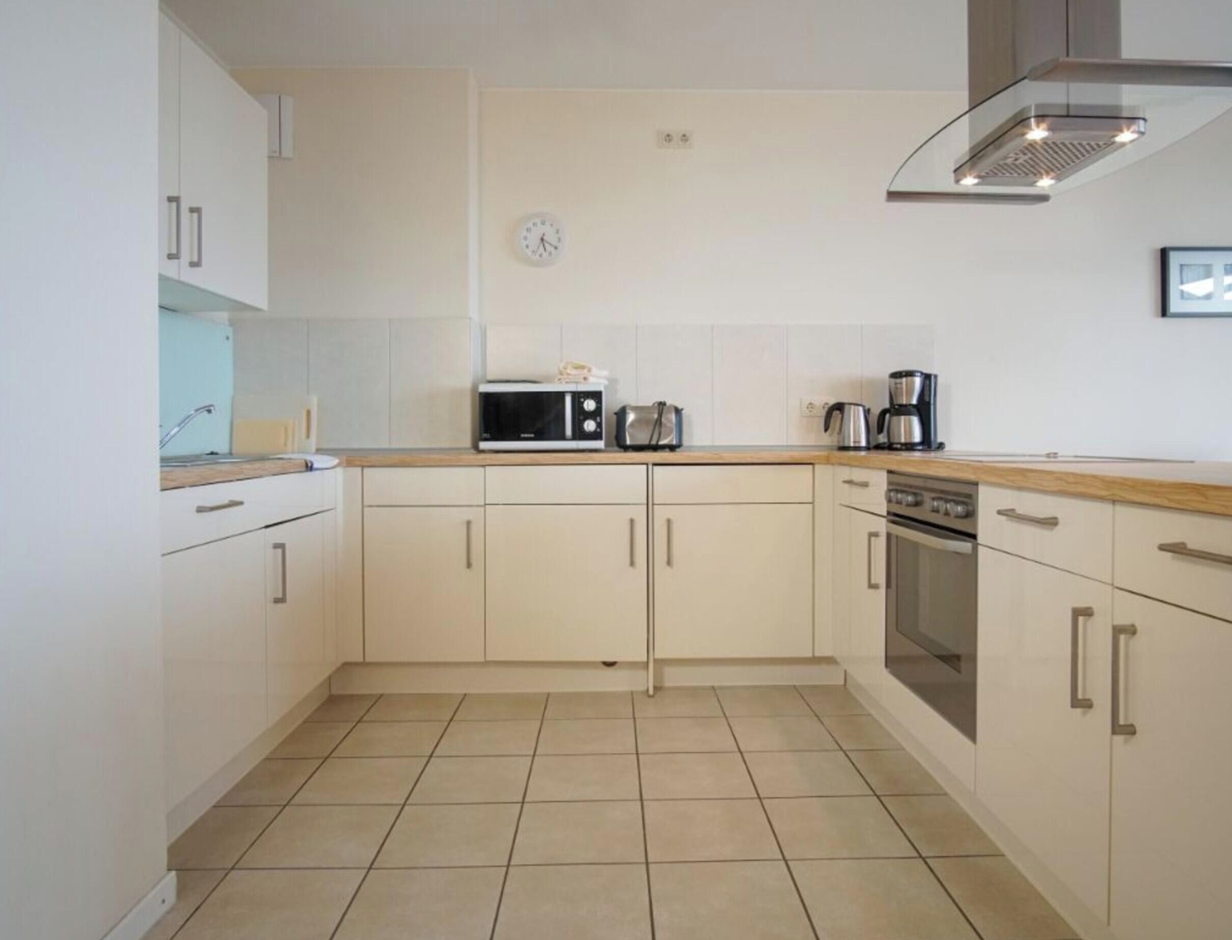 A compact kitchen with white cabinets, a microwave, a kettle, a coffee maker, and a stove.
