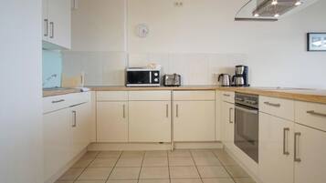 A compact kitchen with white cabinets, a microwave, a kettle, a coffee maker, and a stove.