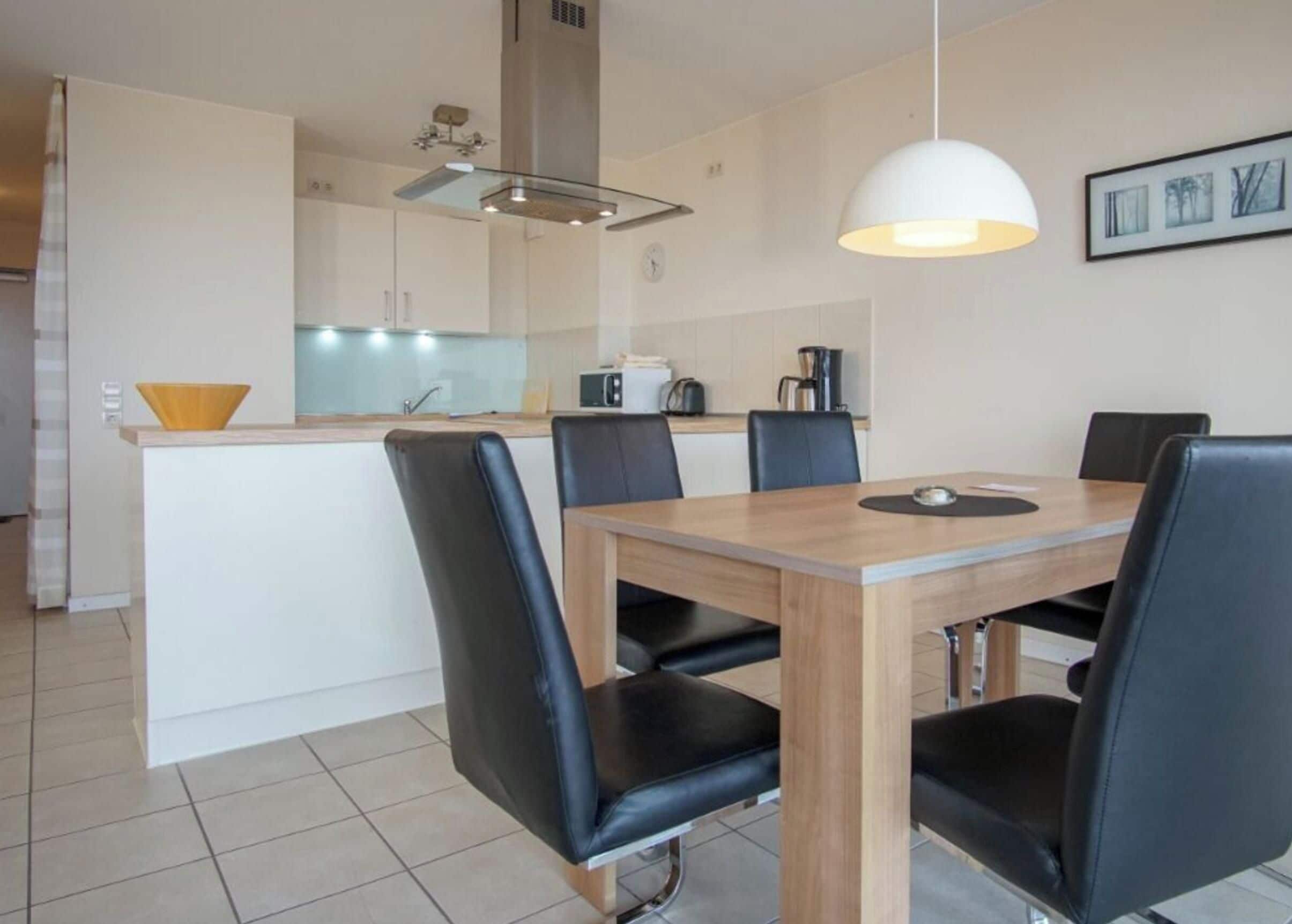 A modern kitchen with a dining area, featuring a wooden table and black chairs.