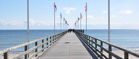 A wooden pier extending into the sea with flags on both sides.