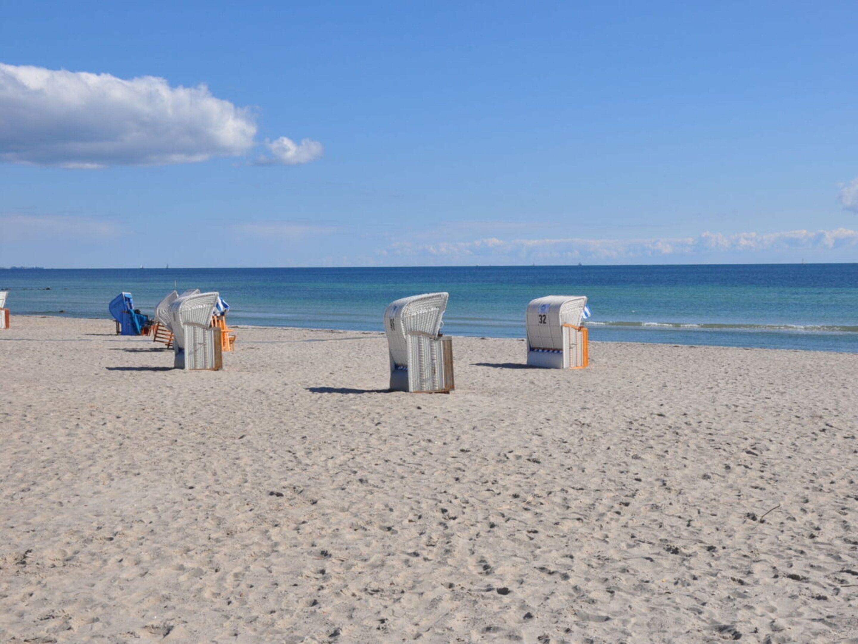 A beach with several wicker beach chairs and a small structure, likely a changing room, on the sand.