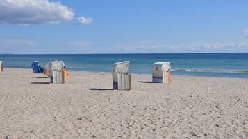 A beach with several wicker beach chairs and a small structure, likely a changing room, on the sand.